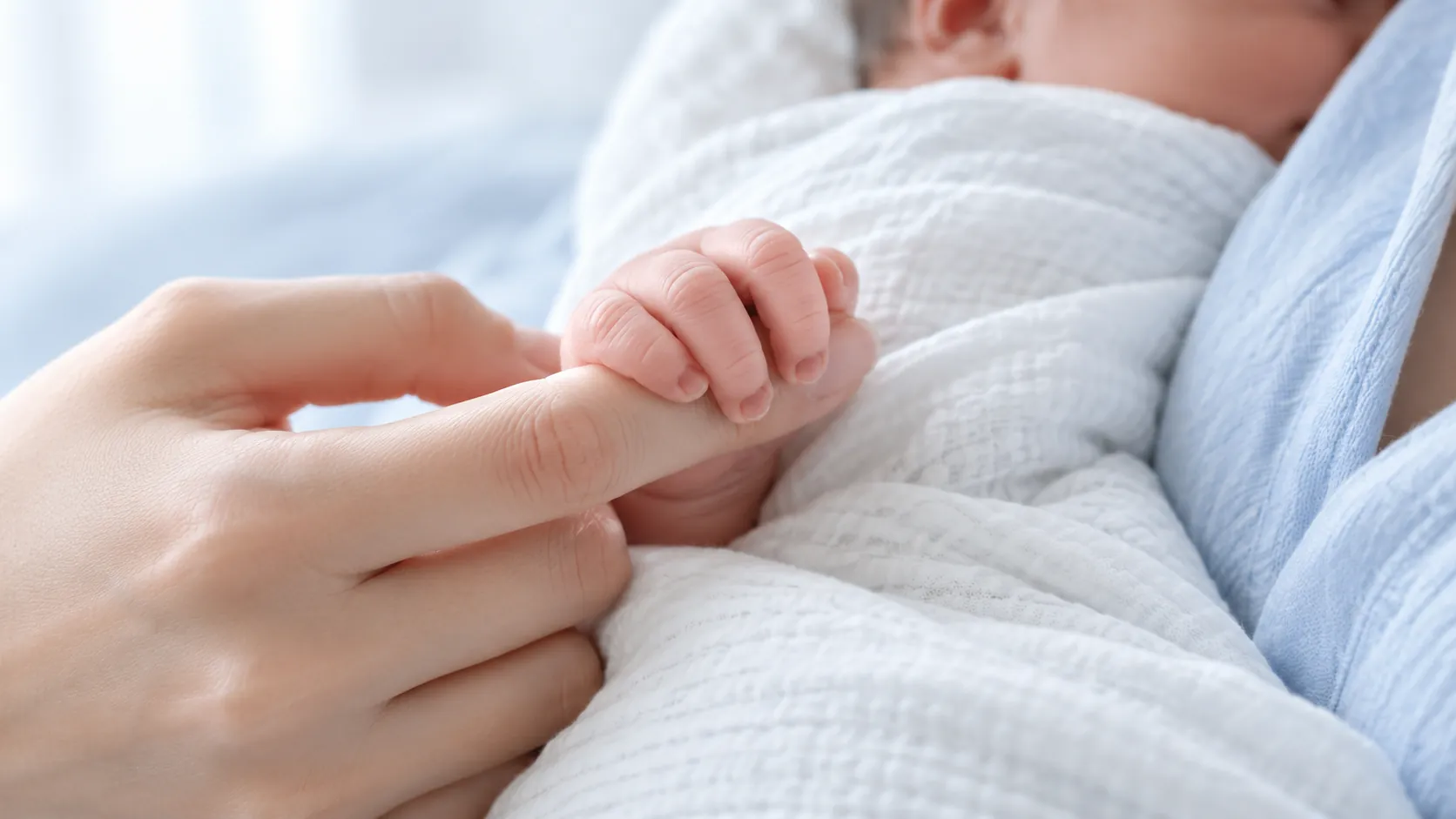 A newborn holding its mother's finger